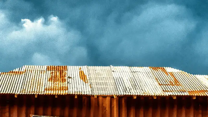Rusted and damaged metal roof under stormy skies, highlighting the importance of pre-hurricane roof inspections.