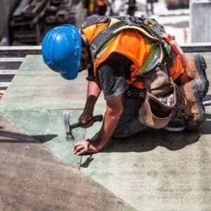 A worker using a hammer to secure roof panels, emphasizing safety and smooth transitions during roof replacement.