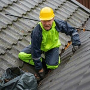 A worker cleaning debris off a roof, demonstrating that there will be different stages involved in the roof replacement and you may need to take different steps to minimize disruptions during different parts of an roof repair project.