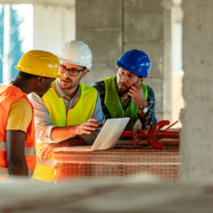 a group of construction professionals in safety gear discussing maintenance plans while reviewing information on a laptop, emphasizing the importance of documenting roof inspections and repairs for insurance compliance and tax deductions.