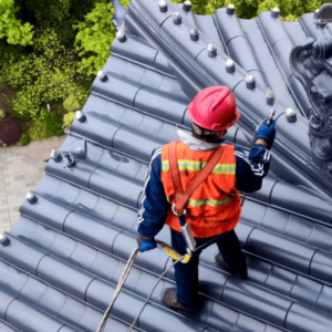 A roofing professional wearing safety gear inspects and applies a sealant on a dark metal roof, highlighting the importance of checking for ponding water and ensuring proper drainage after summer storms.