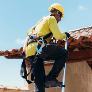 A roofing contractor in safety gear climbs a ladder to inspect and secure a commercial roof, highlighting the importance of hurricane preparedness by reinforcing roofing materials and ensuring structural stability before storm season.