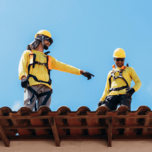 two roofing contractors in safety harnesses inspecting a commercial roof, emphasizing the importance of checking HVAC units and flashing to prevent leaks and ensure proper sealing.