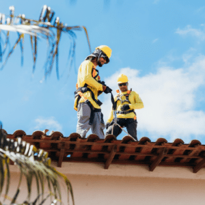 two roofing contractors in safety harnesses inspecting a commercial tile roof under a clear sky, highlighting the importance of a final full inspection before winter to address potential weaknesses and ensure structural integrity.
