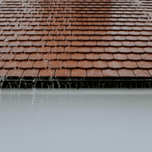 a close-up of a wet shingle roof with rainwater running off the edges, emphasizing the importance of sealing potential leaks before cooler temperatures cause further damage.