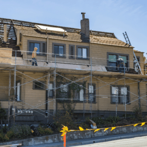 a residential building under renovation with scaffolding and workers repairing the roof, illustrating the challenges of timely roof maintenance and the need for proper planning to avoid costly emergency repairs.