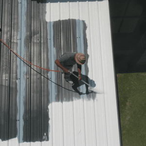 A worker applying a protective roof coating to a commercial metal roof to improve durability and energy efficiency.