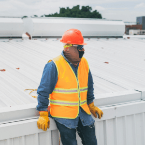 A roofing contractor in safety gear inspecting a commercial metal roof after a storm, highlighting the importance of post-hurricane season inspections to identify and repair potential damage.