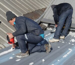 roofing professionals from troyer commercial roofing applying sealant to a metal roof, ensuring durability and leak prevention for long-term protection.