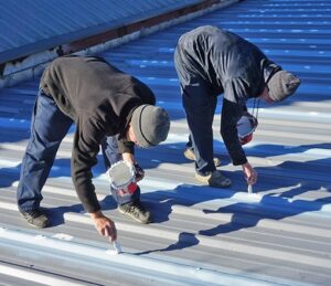 Troyer commercial roofing professionals applying protective sealant to a metal roof, preventing leaks and ensuring long-term durability.