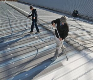 Troyer Commercial Roofing experts applying protective coating on a metal commercial roof, highlighting the value of timely roof maintenance financed without upfront costs.
