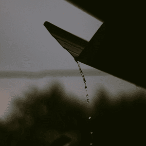 close-up of rainwater dripping from a gutter system, representing water management on flat roofs