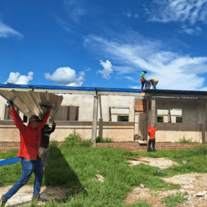 workers installing roofing sheets on a commercial property under sunny skies, demonstrating professional roofing services offering transparent and reliable financing options.