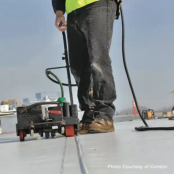 A contractor uses a motorized seam welder to heat weld seams on a commercial flat membrane roof.