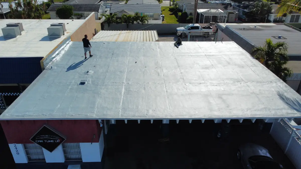 Commercial roofer inspecting a newly coated, flat white roof under clear Florida winter skies during the dry season.