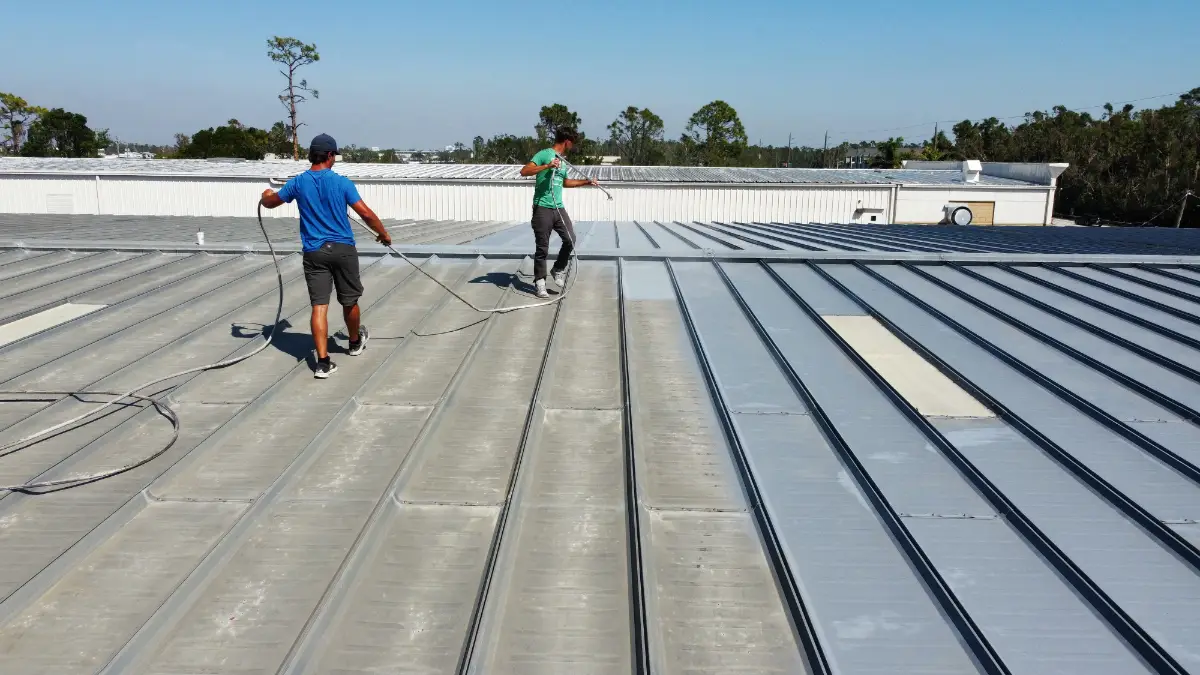 Two roofing technicians applying a roof coating to a metal commercial roof during routine maintenance in Florida. Planning commercial roof maintenance budget