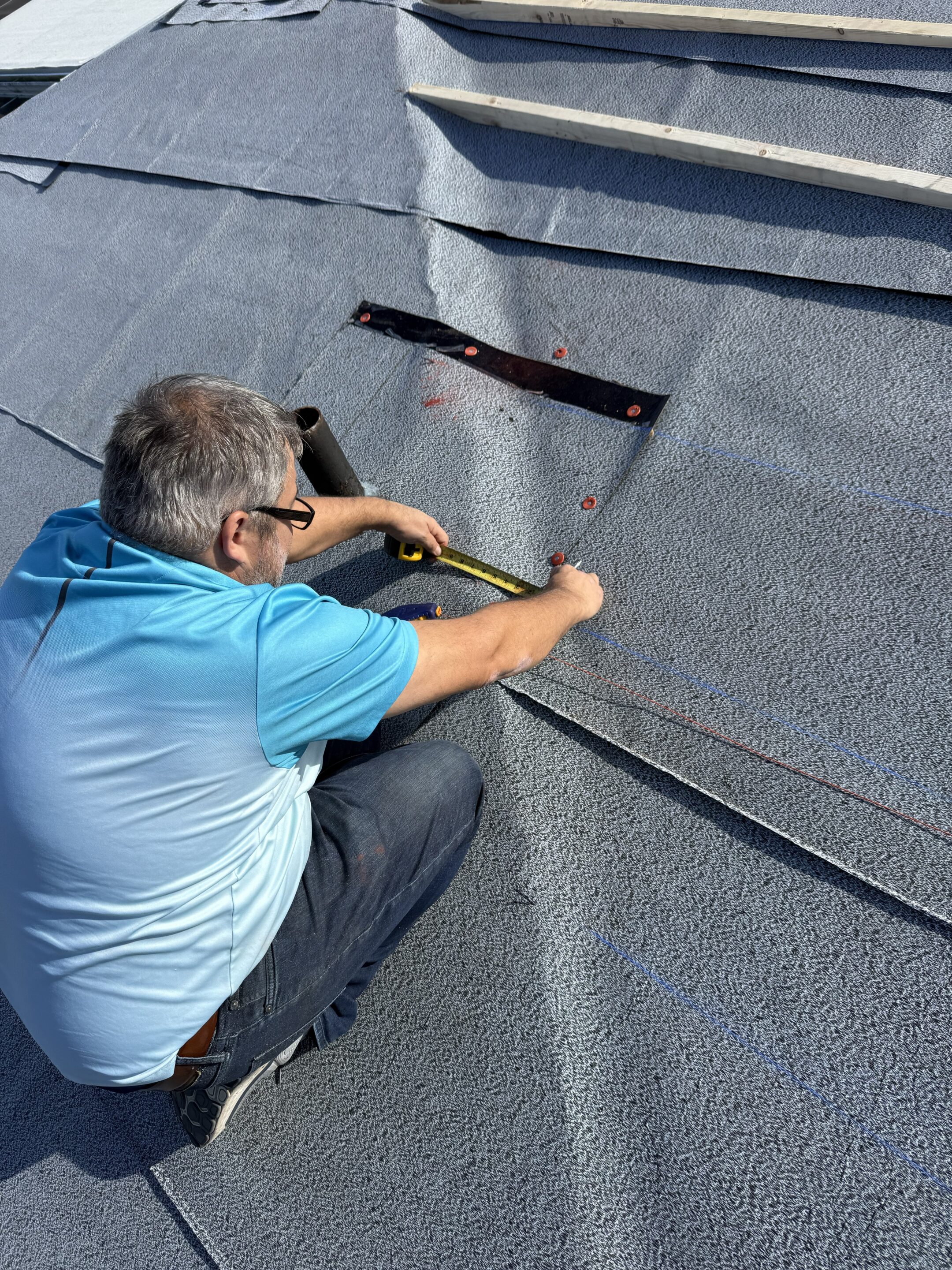 Lester Troyer measuring a repair area beside a pipe penetration on a modified bitumen roof
